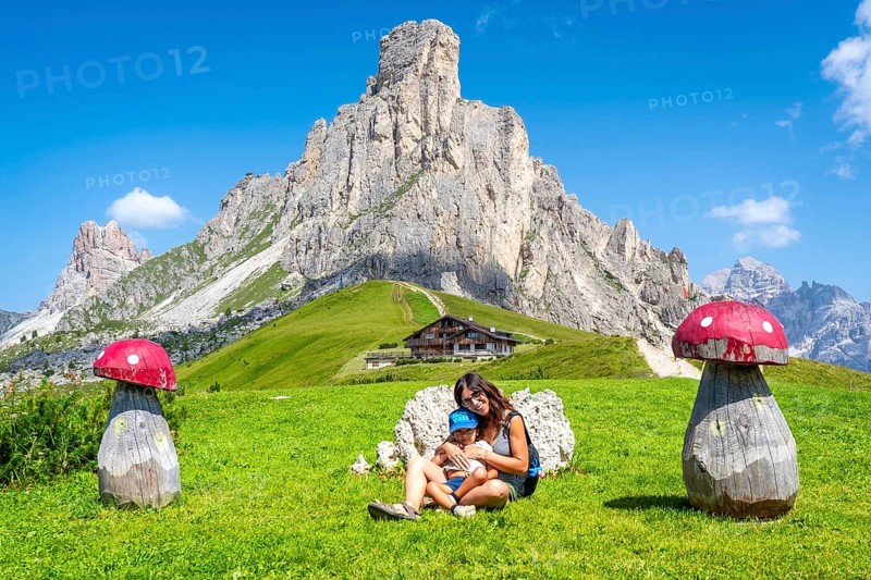 Mother and child relaxing near wooden mushrooms, enjoying breathtaking view of giau pass and surrounding dolomites peaks on sunny summer day