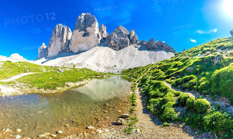 Breathtaking panorama of tre cime di lavaredo reflecting in a crystal clear alpine lake, surrounded by lush meadows on a sunny day