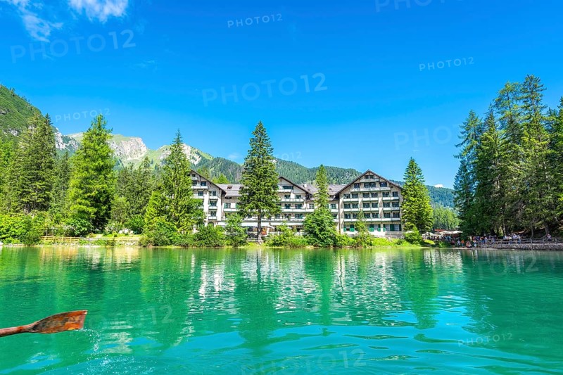 Wooden oar stroking emerald green water of lake braies, with hotel pragser wildsee and dolomites mountains reflected in the tranquil surface