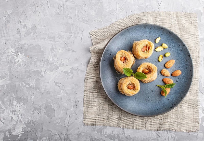 Kunafa, traditional arabic sweets in blue ceramic plate on a gray concrete background. top view, copy space