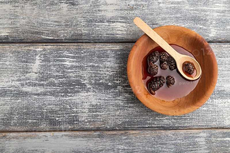 Pine cone jam in wooden bowl on gray wooden background. Top view, flat lay, copy space