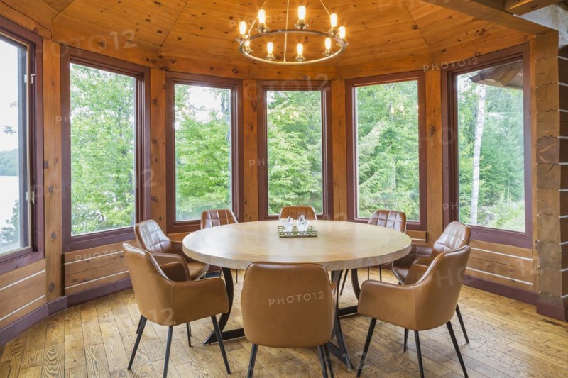 Round wooden dining table with tan leather armchairs in dining room inside a milled Eastern white pine timber and flat log profile home, Quebec, Canada, North America