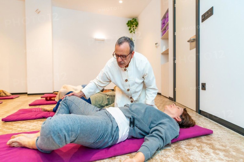 Qi gong male teacher dressed with traditional wa tung correcting a woman during meditation class