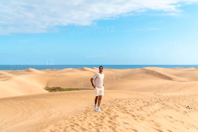 Tourist exploring the scenic landscape of maspalomas dunes with the ocean in the background