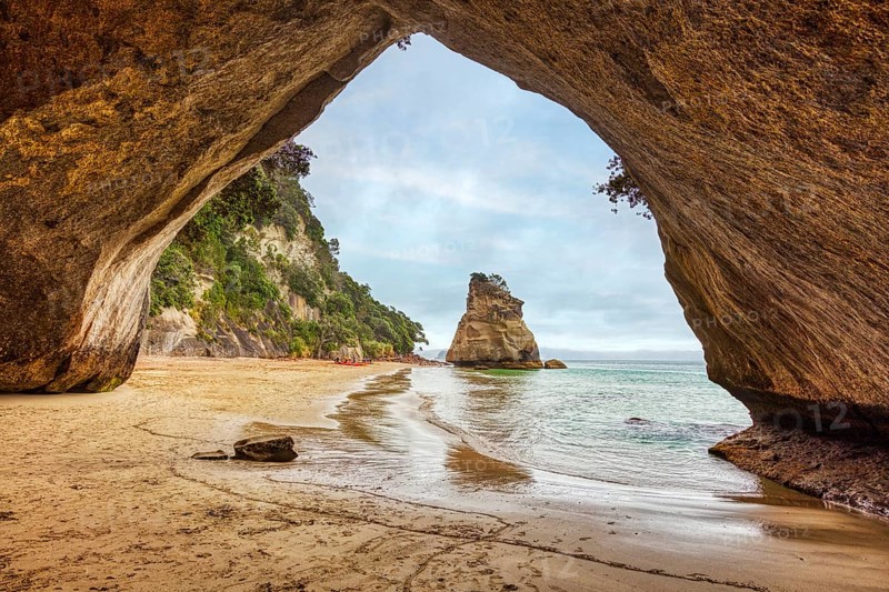 Looking out of a cave onto a rock formation and a quiet beach, Cathedral Grove, Coromandel, New Zealand, Oceania