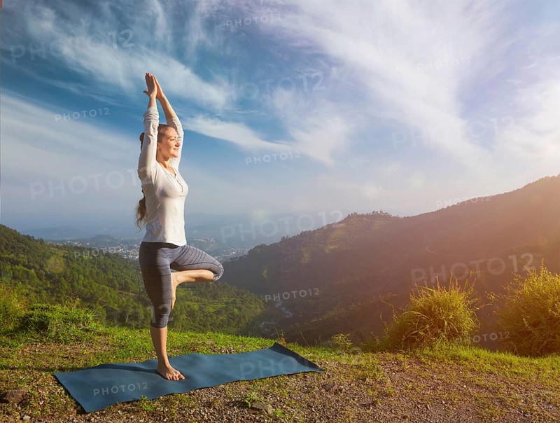 Yoga practice outdoors, woman practices balance yoga asana Vrikshasana tree pose in Himalayas mountains outdoors in the morning. Himachal Pradesh, India, Asia
