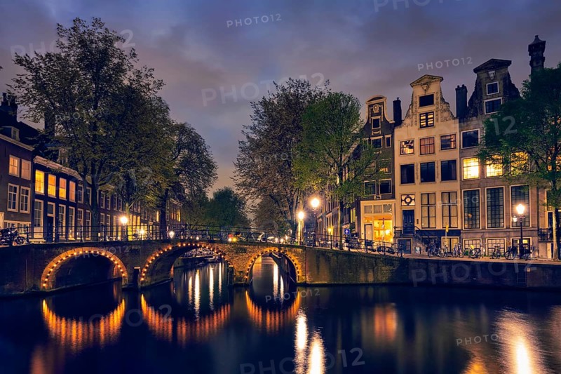 Night view of Amterdam cityscape with canal, bridge and medieval houses in the evening twilight illuminated. Amsterdam, Netherlands