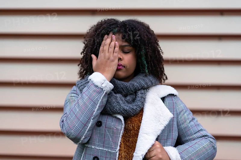 Black ethnic woman making a stop racism gesture on a gray wall, covering her eyes