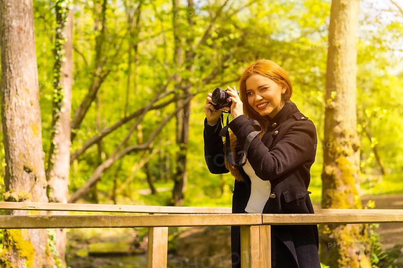 Woman photographer with a black jacket enjoying in an autumn park, taking pictures at sunset on a wooden bridge