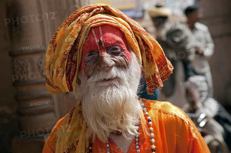 Old Hare Krishna follower dressed in orange dress in front of temple in Govardhan, India, Asia