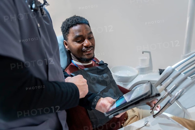 Dentist showing a dental x ray on a tablet to a smiling patient during a consultation in a modern dental clinic