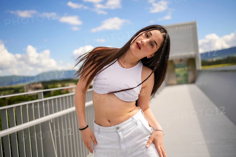 Caucasian young sportive woman moving sensually looking at camera while performing urban dance on an outdoor bridge