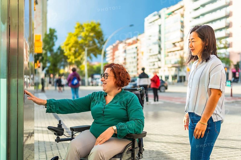 Disabled woman in a wheelchair and Asian friend waiting for the public transport elevator