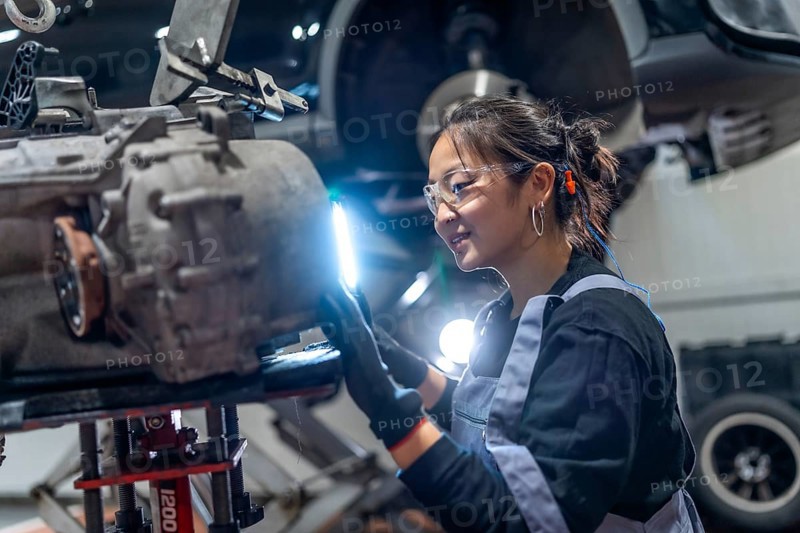 Skilled female mechanic wearing safety glasses and earplugs, meticulously inspecting a gearbox in a professional auto repair shop