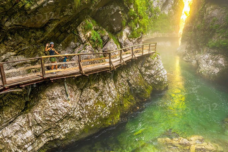 Tourists enjoying a scenic walk along the wooden pathway above the emerald radovna river, surrounded by the steep cliffs of vintgar gorge