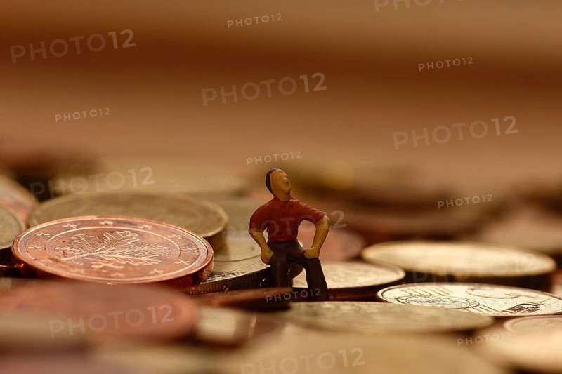 Miniature man sitting among euro coins, North Rhine-Westphalia, Germany, Europe