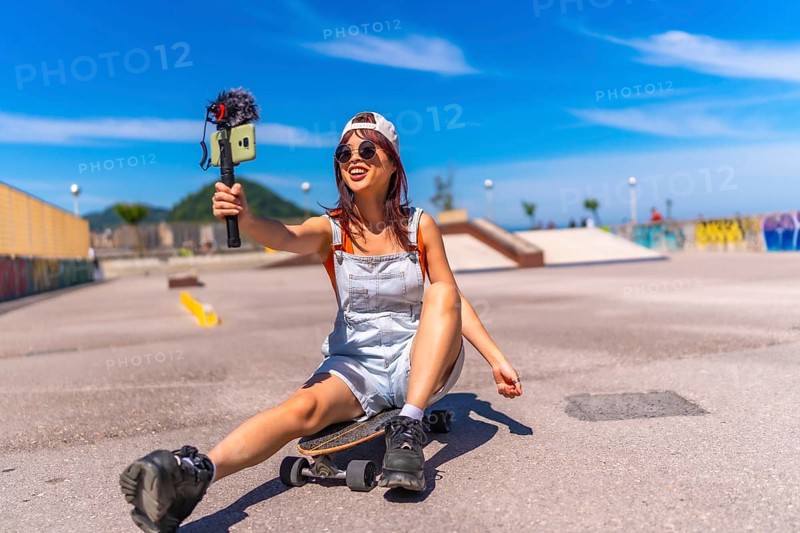 Smiling chinese female vlogger filming at skateboard park in summer