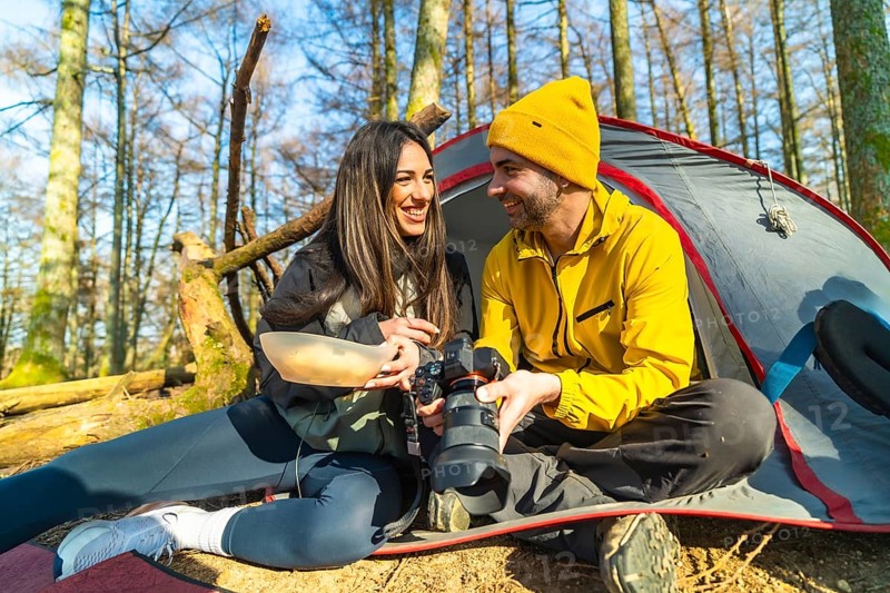Couple of photographers camping and having a meal while reviewing photos they have taken in the forest