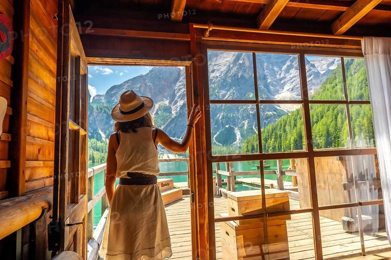 Tourist wearing straw hat looking at the amazing landscape of lake braies from the wooden hut on the pier