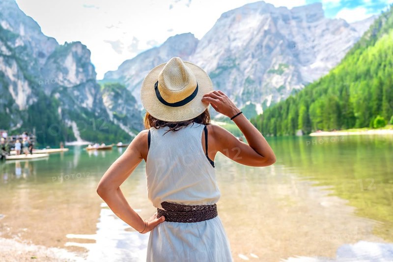 Woman wearing straw hat, enjoying the amazing view of lake braies in the dolomites mountains during summer