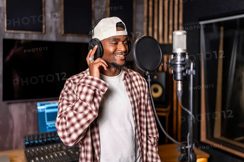 Young happy african american male singer wearing headphones and recording a song in professional music studio