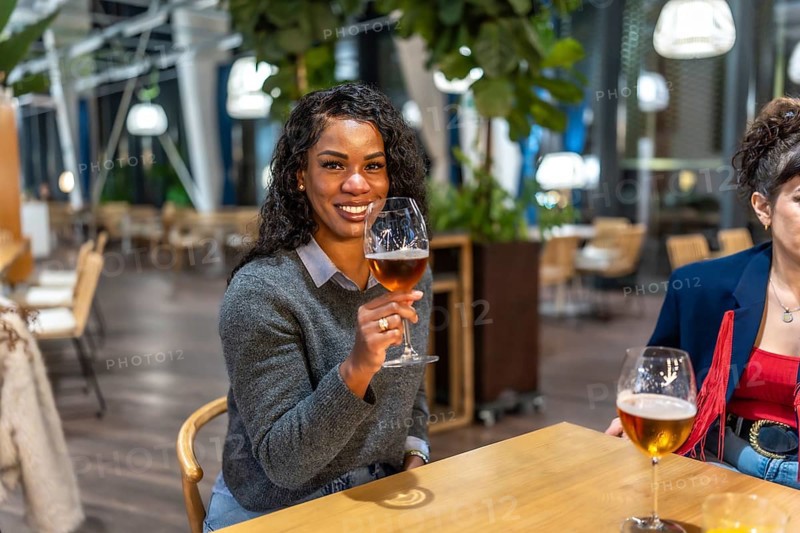 Latin woman enjoying beer talking to friends sitting on the terrace of a night bar