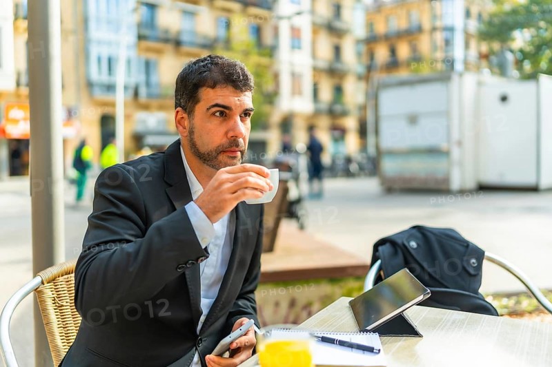 Businessman enjoying morning coffee while working with smartphone and digital tablet in an outdoor cafeteria