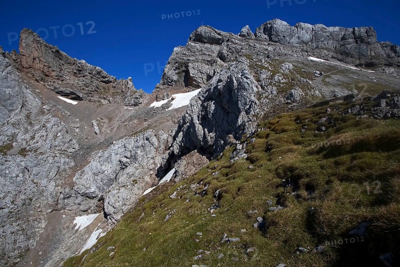Steep mountain face with scattered snow fields and green grassy areas under a clear sky, Karwendel, Mittenwald, Bavaria, Germany, Europe