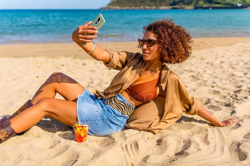 Confident woman in summer clothes taking selfie leaning on sandy beach