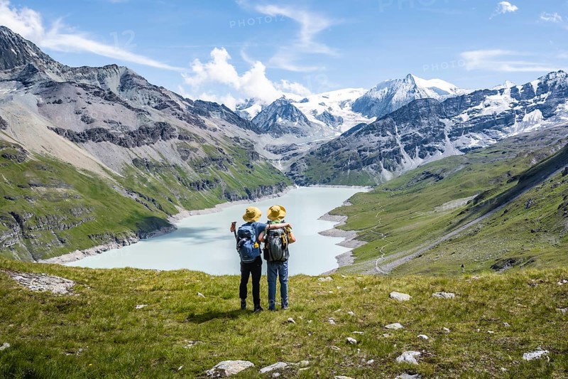 Two friends with yellow hats, mountaineers in front of a blue mountain lake, reservoir Lac des Dix, behind mountain peak Mont Blanc de Cheilon with glacier, Hérménence, Valais Alps, Valais, Switzerland, Europe