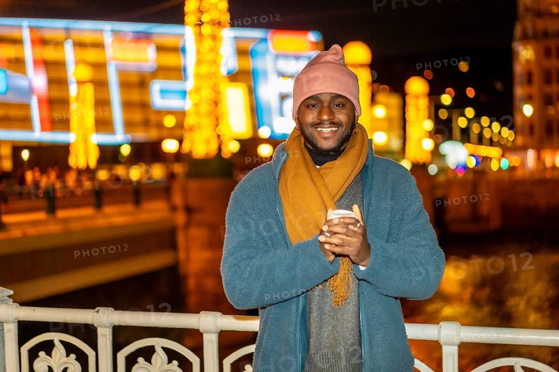 Smiling african man holding a warm cup of coffee in the city in a Christmas season night