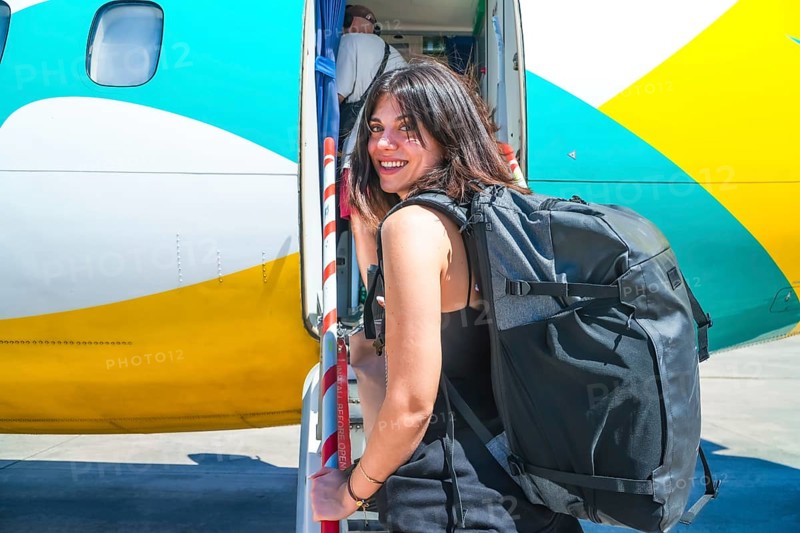 Female tourist exiting airplane after landing in philippines airport, carrying backpack and smiling