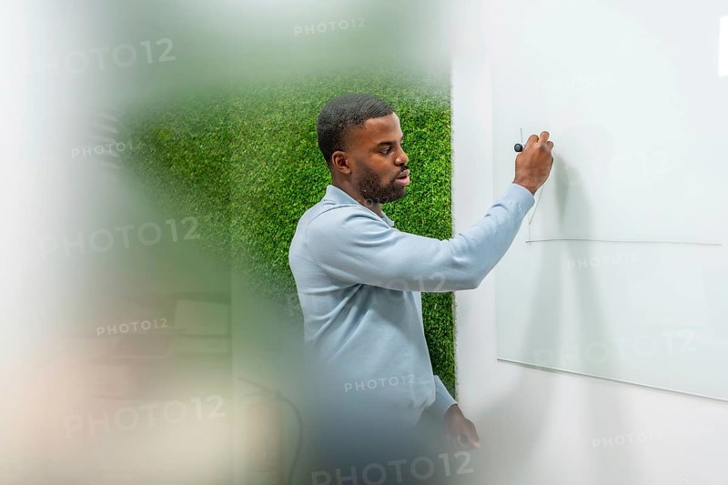 Manager drawing graph on whiteboard during a presentation in modern coworking office with green wall