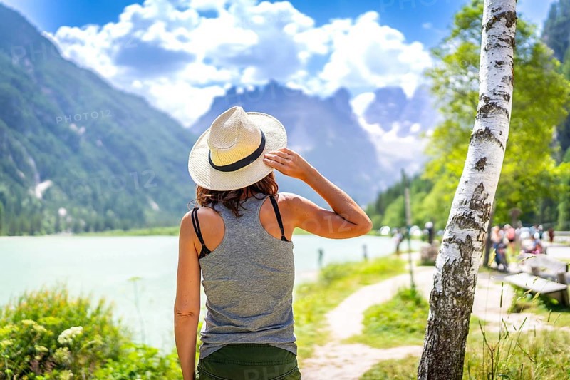 Woman wearing straw hat enjoying the view of the beautiful lago di landro with the dolomites in the background on a summer day, italy
