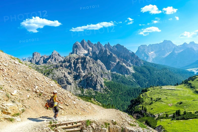 Female tourist hiking on a mountain trail with breathtaking views of the tre cime di lavaredo peaks in the italian dolomites on a sunny summer day