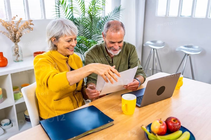 Senior couple going over bills with laptop sitting in the living room with coffee cup
