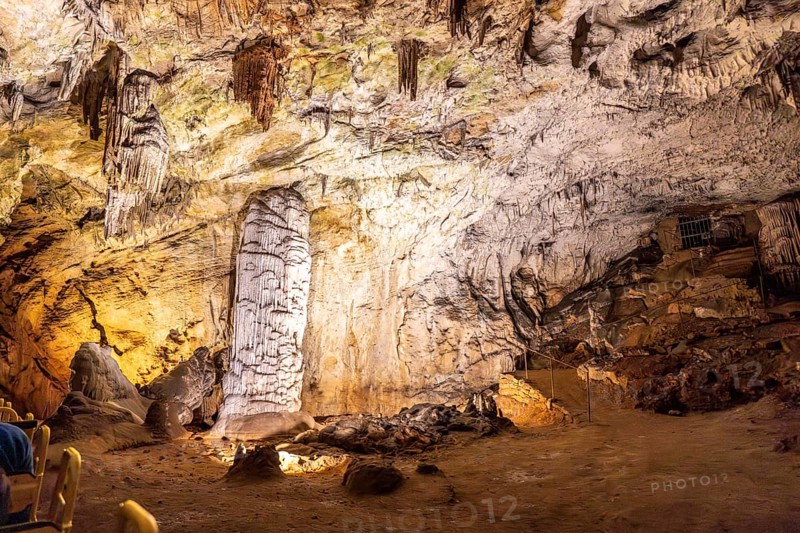 Tourists riding a train admiring the illuminated stalagmites and stalactites inside the famous postojna cave, a popular destination in slovenia