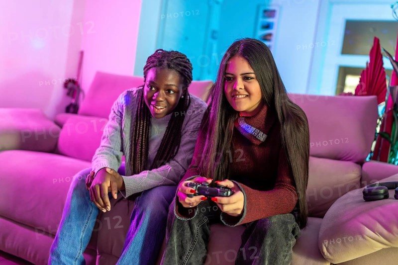 Two friends enjoying their free time playing with a gamepad sitting on a sofa in a colorful living room