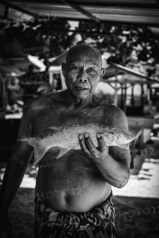 Indonesian fishmonger at a market, fish, man, food, foodstuff, local, travel, long distance, portrait, human, single, free upper body, presents, holding, showing, shows, catch, fishing, seafood, looking, joyful, market, trade, exotic, market stall, fresh, animal, sea, sea animal, black and white, monochrome, travel photo, Bali, Indonesia, Asia