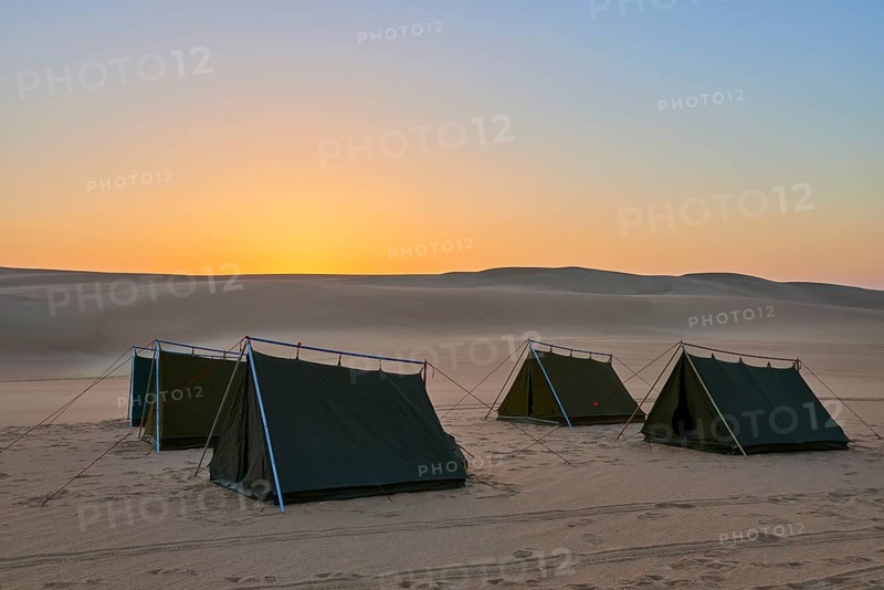 Four tents stand in a vast desert at dusk, surrounded by sand dunes under an orange-coloured sky, Matruh, Great Sand Sea, Libyan Desert, Sahara, Egypt, North Africa, Africa