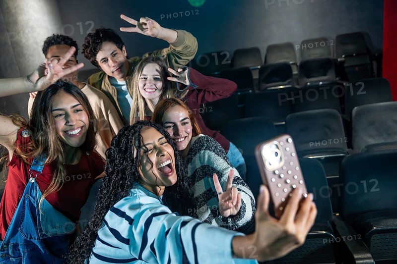 Group of cheerful young friends taking selfie at movie theater or disco party, making victory signs and enjoying entertainment event