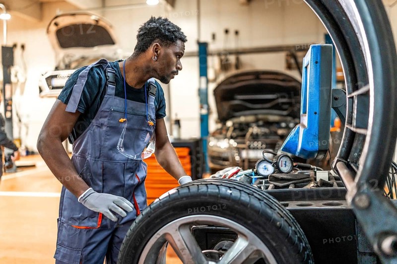 Professional mechanic using a digital tire pressure gauge during a wheel maintenance procedure in a busy car workshop