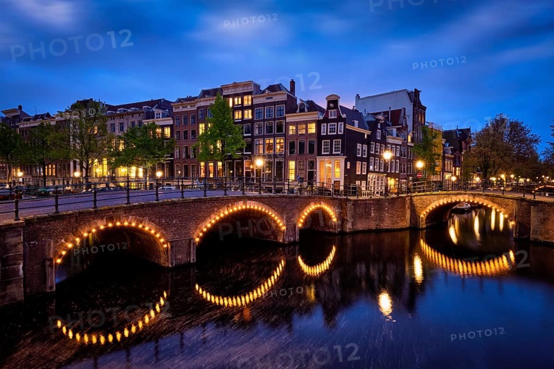 Night view of Amsterdam cityscape with canal, bridge and medieval houses in the evening twilight illuminated. Amsterdam, Netherlands
