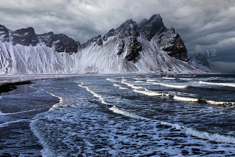 White foamy waves on the beach of Stokkness, behind snowy rocky slopes of Vestrahorn, near Höfn, Sudausturland, Iceland, Europe