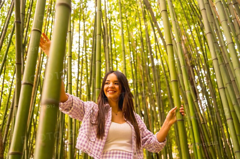 Young caucasian girl with a pink skirt in a bamboo forest. Enjoying summer holidays in a tropical climate, walking in the forest grabbing the trunks of bamboo and smiling