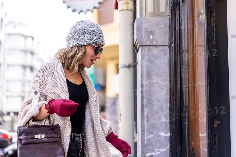 Young Caucasian blonde girl shopping in the city in winter, looking at clothing stores. Sunglasses and red gloves