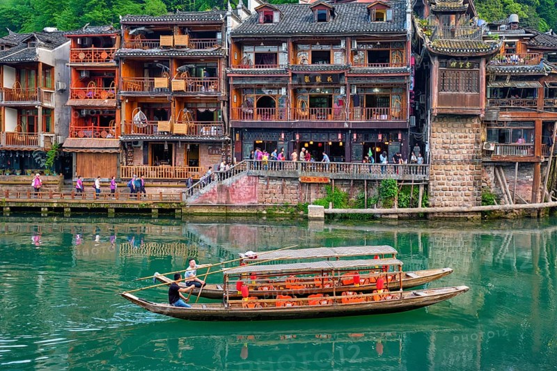FENGHUANG, CHINA, APRIL 21, 2018: Chinese tourist attraction destination, Feng Huang Ancient Town (Phoenix Ancient Town) on Tuo Jiang River with bridge and tourist boat. Hunan Province, China, Asia