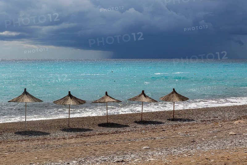 Line of sunshades along the beach with dark storm clouds offshore, Dhermi, Albania, Europe