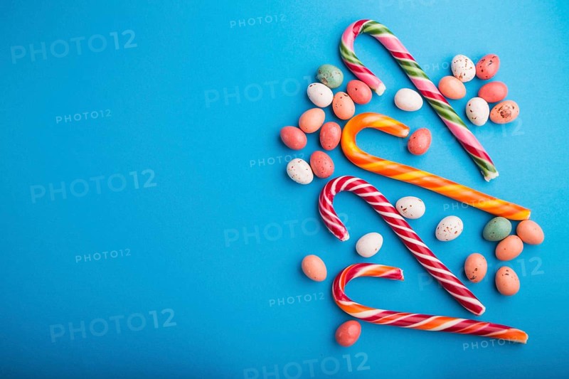 Colorful multicolored candies on a blue background. Christmas cane, chocolate eggs, caramel dragees. copy space, top view, flat lay