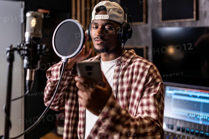 Young man recording vocals for new hit album in professional music studio, using pop filter and headphones